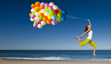 girl running on beach with lots of balloons