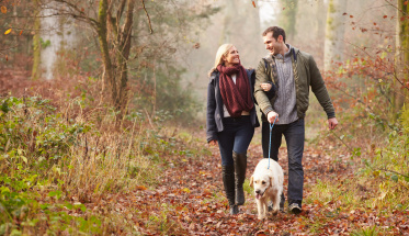 Couple Walking Dog Through Winter Woodland